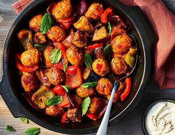 One pot harissa Quorn meatballs served in a black dish with crème fraiche on the side.