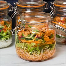A row of glass jars with hinged lids, each filled with layers of rice noodles, vegetables, and Quorn chicken pieces.